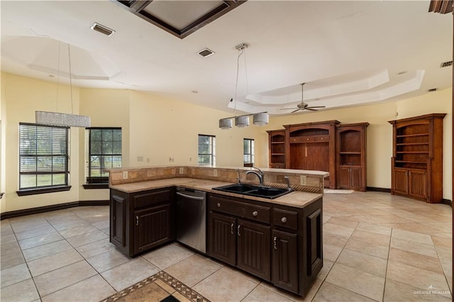 kitchen featuring dishwasher, sink, a raised ceiling, pendant lighting, and a center island with sink