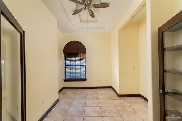 tiled empty room with a tray ceiling and ceiling fan