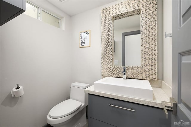 bathroom featuring vanity, toilet, and backsplash