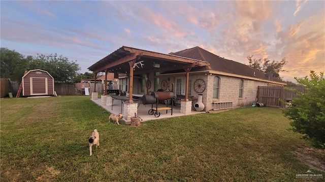 back house at dusk featuring a yard, a patio, and a shed