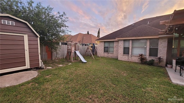 yard at dusk featuring a playground and a storage unit