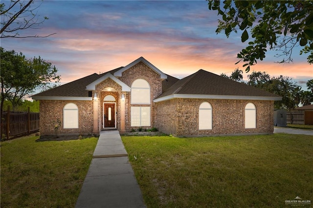 view of front of home with a front lawn, fence, brick siding, and a shingled roof