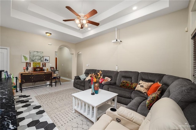 living room featuring a tray ceiling, arched walkways, and a ceiling fan