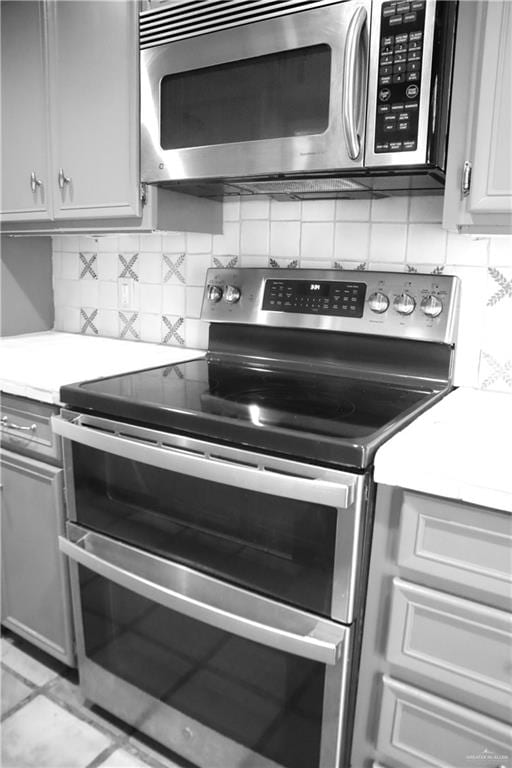 kitchen featuring gray cabinets, light tile patterned floors, stainless steel appliances, and tasteful backsplash