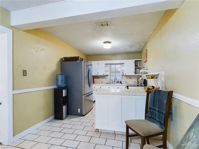 kitchen with tile countertops, stainless steel appliances, visible vents, white cabinets, and a sink