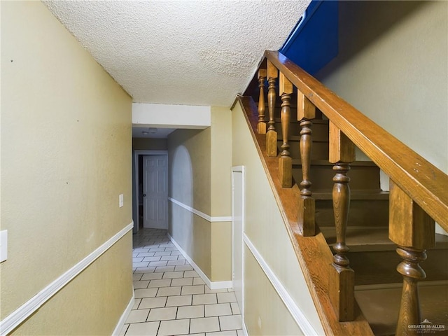 stairway with a textured ceiling, baseboards, and tile patterned floors