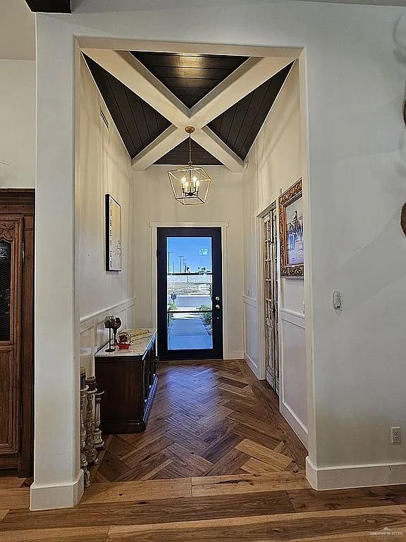 doorway with a notable chandelier, beamed ceiling, coffered ceiling, and baseboards