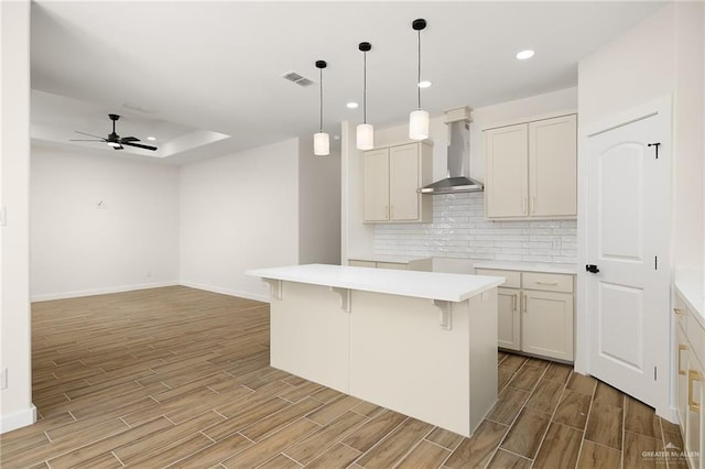 kitchen with wood finished floors, ceiling fan, backsplash, wall chimney exhaust hood, and visible vents