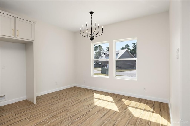 unfurnished dining area featuring a chandelier, light wood finished floors, and baseboards