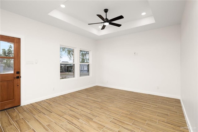 unfurnished room with baseboards, a ceiling fan, a tray ceiling, and light wood-type flooring