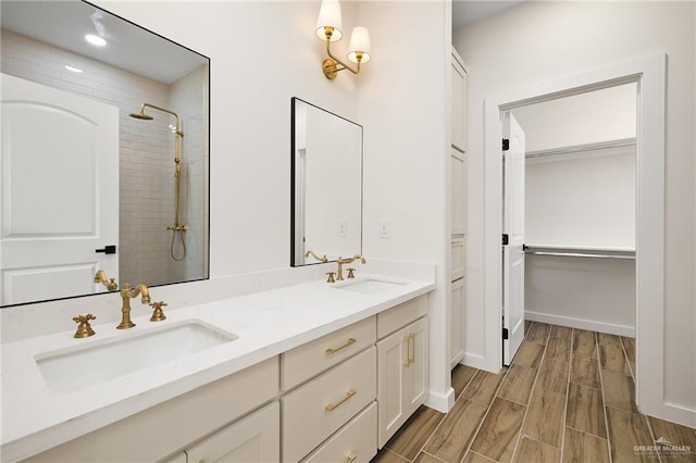 full bath featuring a walk in closet, a tile shower, double vanity, and a sink