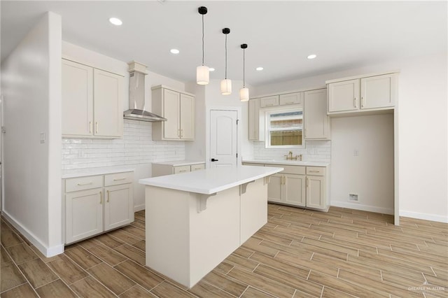 kitchen with tasteful backsplash, wood finish floors, wall chimney exhaust hood, baseboards, and a kitchen island