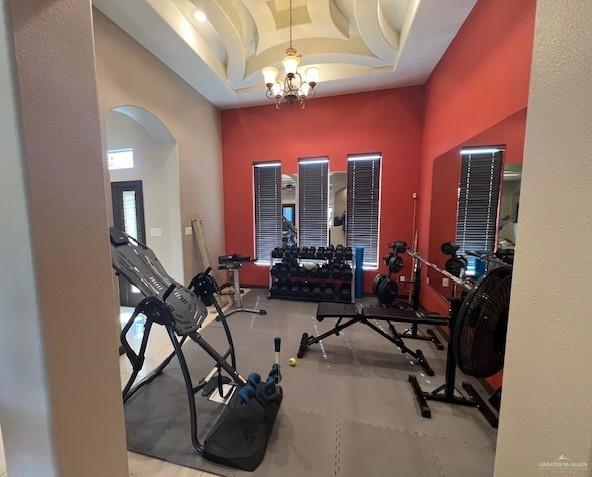 exercise area featuring a high ceiling, a raised ceiling, and a notable chandelier