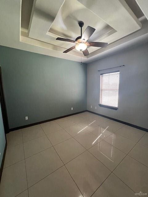 empty room with ceiling fan, a raised ceiling, and light tile patterned floors