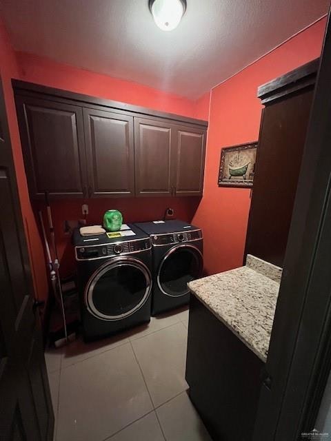 laundry room featuring washing machine and dryer, light tile patterned floors, and cabinets