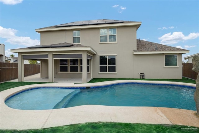 rear view of property featuring solar panels, a patio, and a fenced in pool