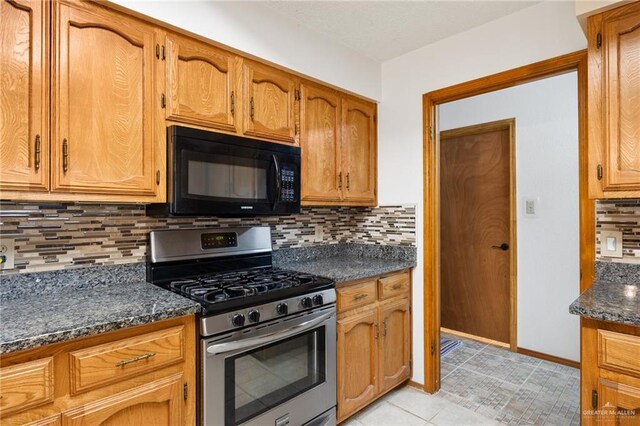 kitchen with tasteful backsplash, dark stone countertops, light tile patterned flooring, and stainless steel range with gas stovetop