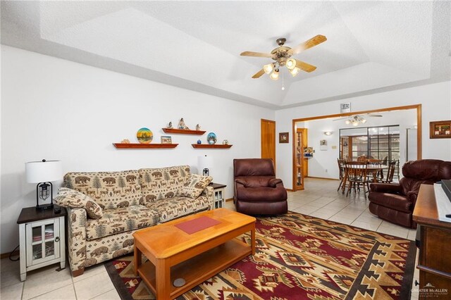 tiled living room with a raised ceiling and ceiling fan