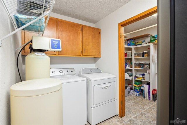 washroom with cabinets, a textured ceiling, and washing machine and clothes dryer