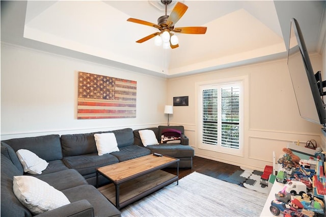 living room featuring hardwood / wood-style flooring, ceiling fan, a raised ceiling, and ornamental molding