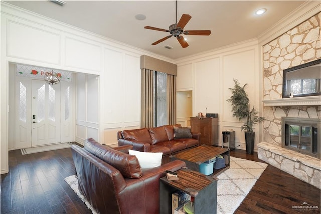 living room featuring ceiling fan, a stone fireplace, ornamental molding, and dark wood-type flooring