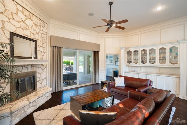 living room featuring dark hardwood / wood-style floors, ceiling fan, ornamental molding, and a fireplace