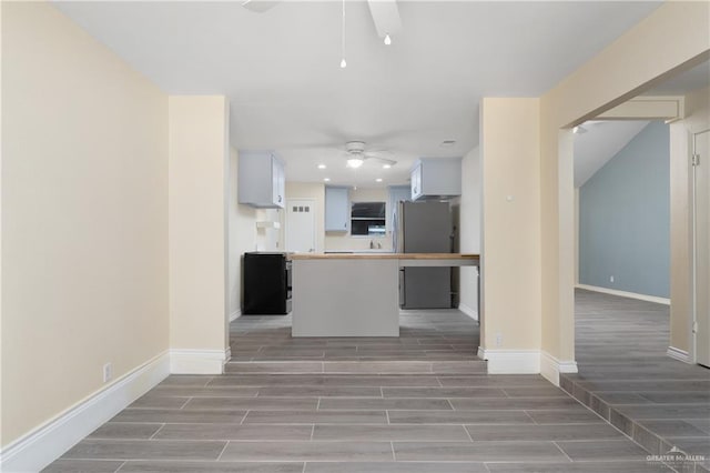 kitchen featuring stainless steel fridge, ceiling fan, wood-type flooring, white cabinets, and a center island