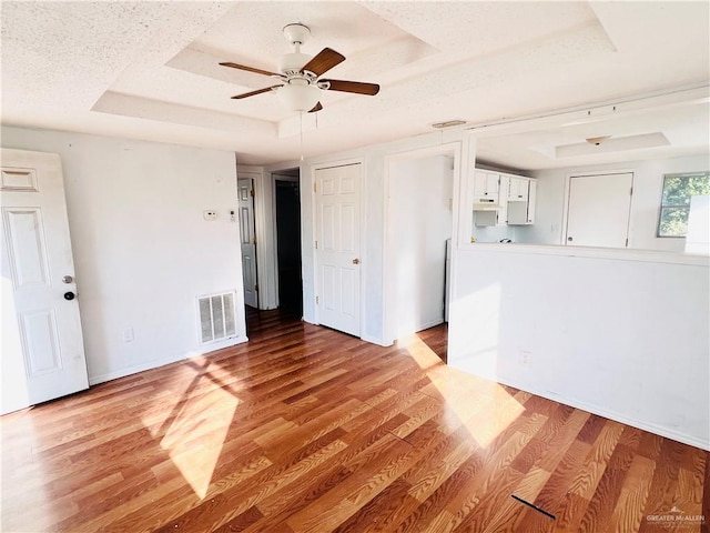 empty room with ceiling fan, a raised ceiling, and light hardwood / wood-style flooring