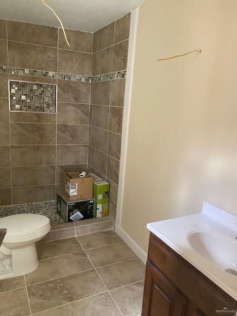 bathroom with a tile shower, vanity, toilet, and tile patterned floors