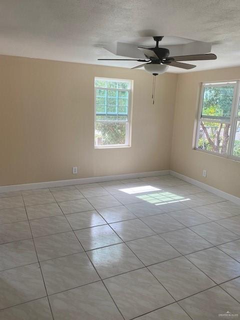 spare room with light tile patterned floors, a textured ceiling, a wealth of natural light, and ceiling fan