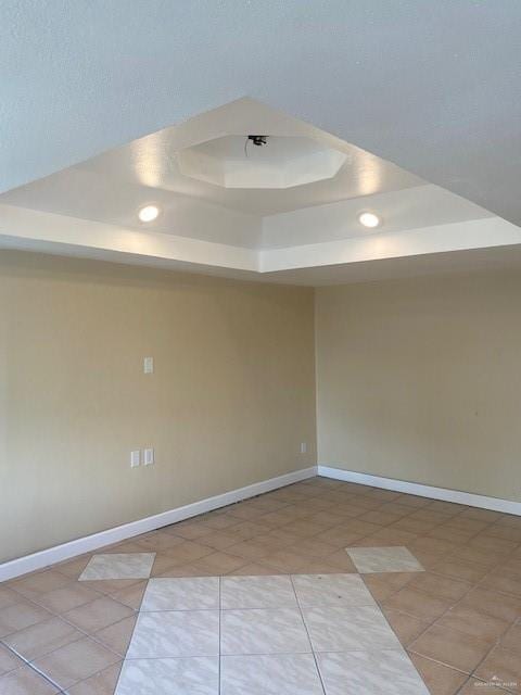 empty room with light tile patterned floors and a tray ceiling