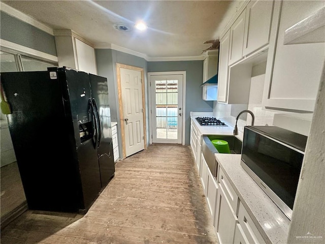 kitchen featuring white cabinets, appliances with stainless steel finishes, wood finished floors, crown molding, and wall chimney range hood