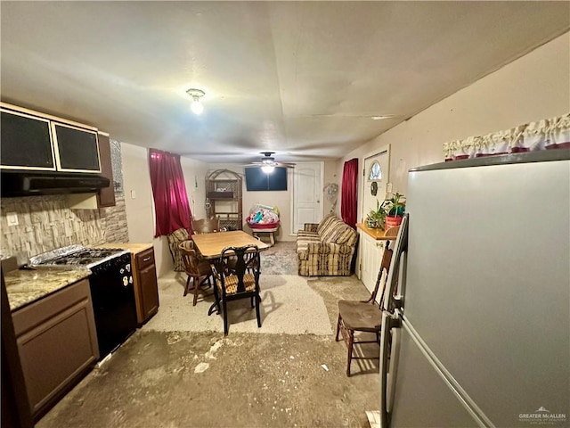 kitchen featuring light countertops, black range with gas stovetop, a ceiling fan, freestanding refrigerator, and under cabinet range hood