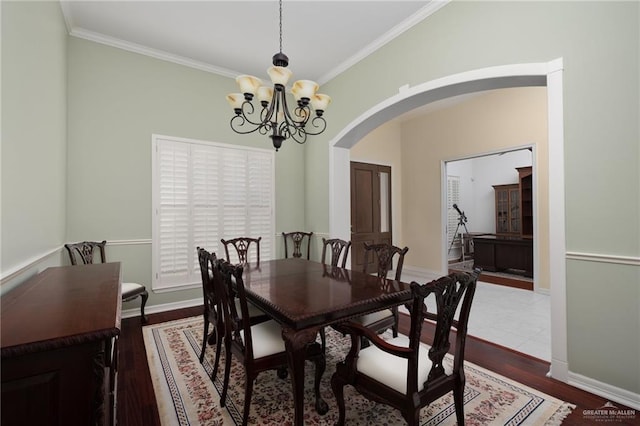 dining room with a notable chandelier, ornamental molding, wood finished floors, arched walkways, and baseboards