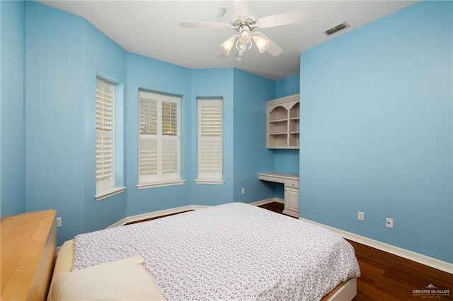 bedroom with visible vents, dark wood-type flooring, built in desk, baseboards, and ceiling fan