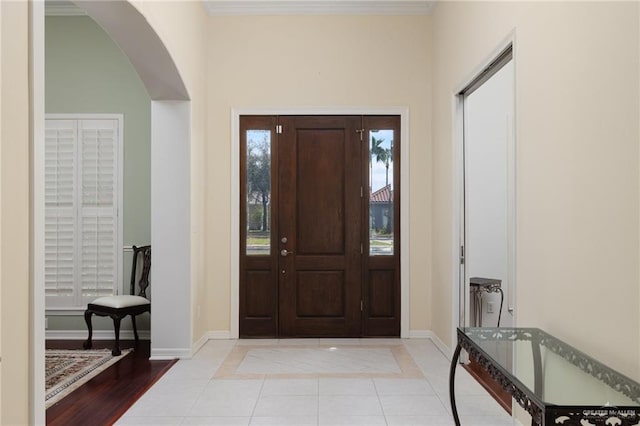 foyer entrance with light tile patterned floors, arched walkways, baseboards, and ornamental molding