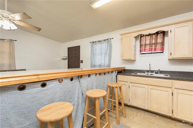 kitchen featuring a ceiling fan, dark countertops, a breakfast bar, light brown cabinets, and a sink