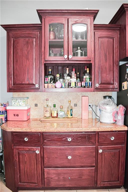 bar featuring black refrigerator, light stone countertops, and backsplash