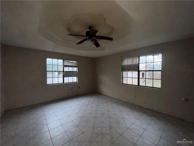 spare room featuring a raised ceiling, ceiling fan, and a healthy amount of sunlight