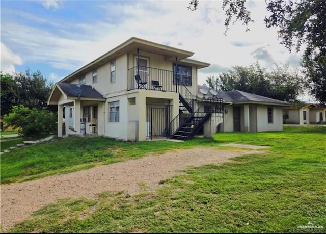 rear view of house with driveway, stairs, a lawn, and stucco siding