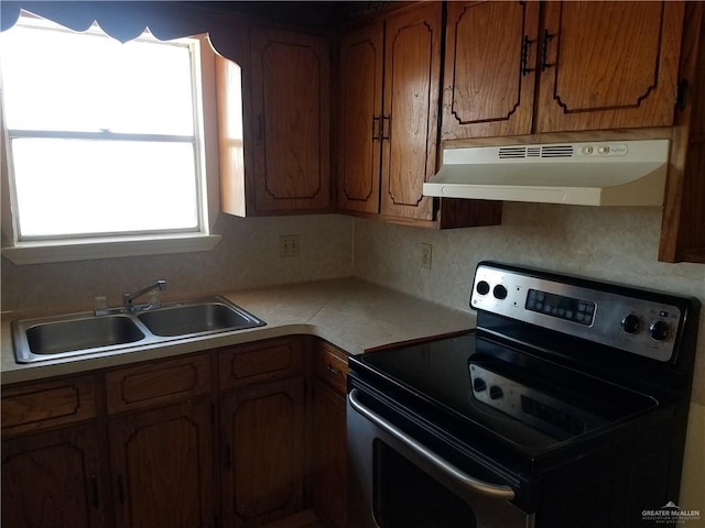 kitchen featuring brown cabinets, stainless steel electric range oven, light countertops, a sink, and under cabinet range hood