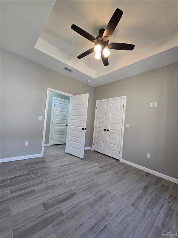 1204 Cornerstone Loop, Rio Grande City, TX 78582 - unfurnished bedroom featuring wood finish floors, visible vents, ceiling fan, a tray ceiling, and baseboards