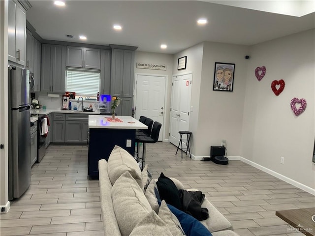 kitchen featuring gray cabinets, stainless steel refrigerator, sink, a center island, and black / electric stove