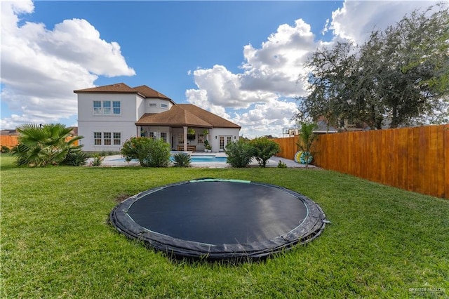 rear view of property featuring a trampoline, a fenced in pool, and a lawn