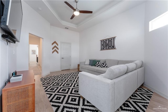 living room featuring a raised ceiling, a high ceiling, ceiling fan, and light hardwood / wood-style flooring