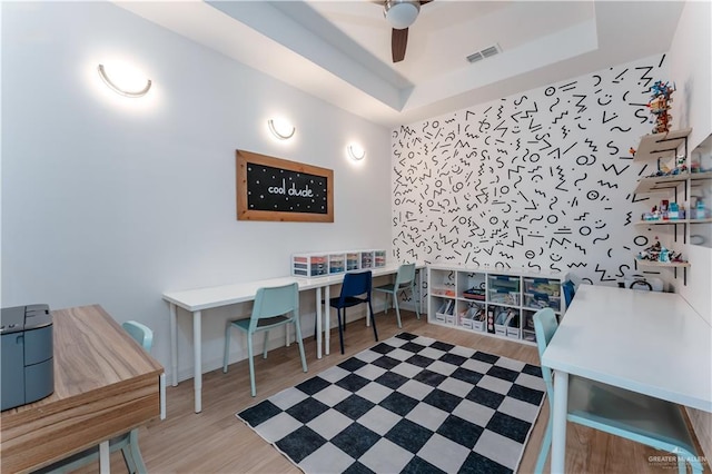 office featuring a raised ceiling, light wood-type flooring, and ceiling fan