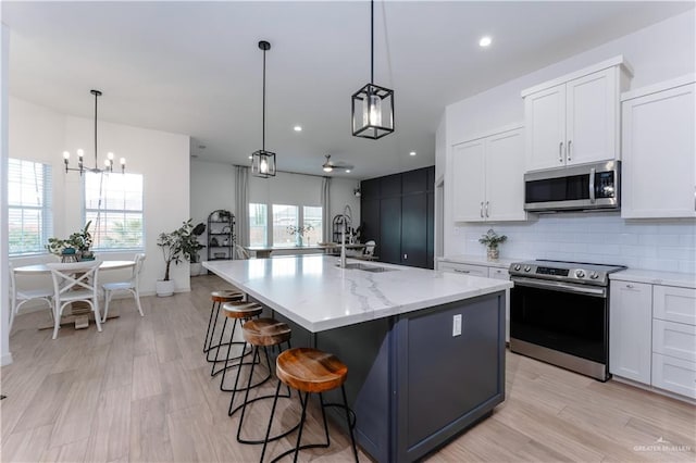 kitchen with pendant lighting, backsplash, stainless steel appliances, an island with sink, and white cabinets