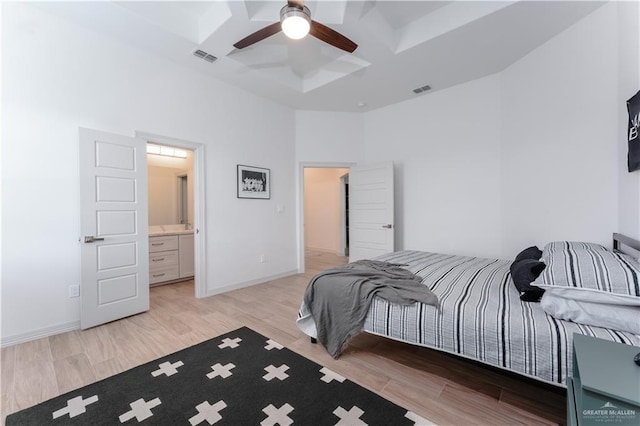 bedroom featuring ceiling fan, a towering ceiling, ensuite bathroom, coffered ceiling, and light wood-type flooring