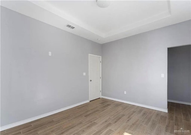 empty room featuring a tray ceiling, baseboards, and wood finished floors