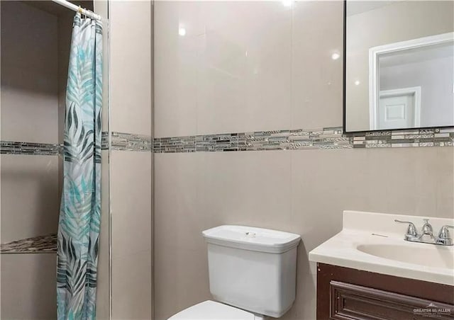 full bathroom with vanity, tile walls, toilet, and a tile shower